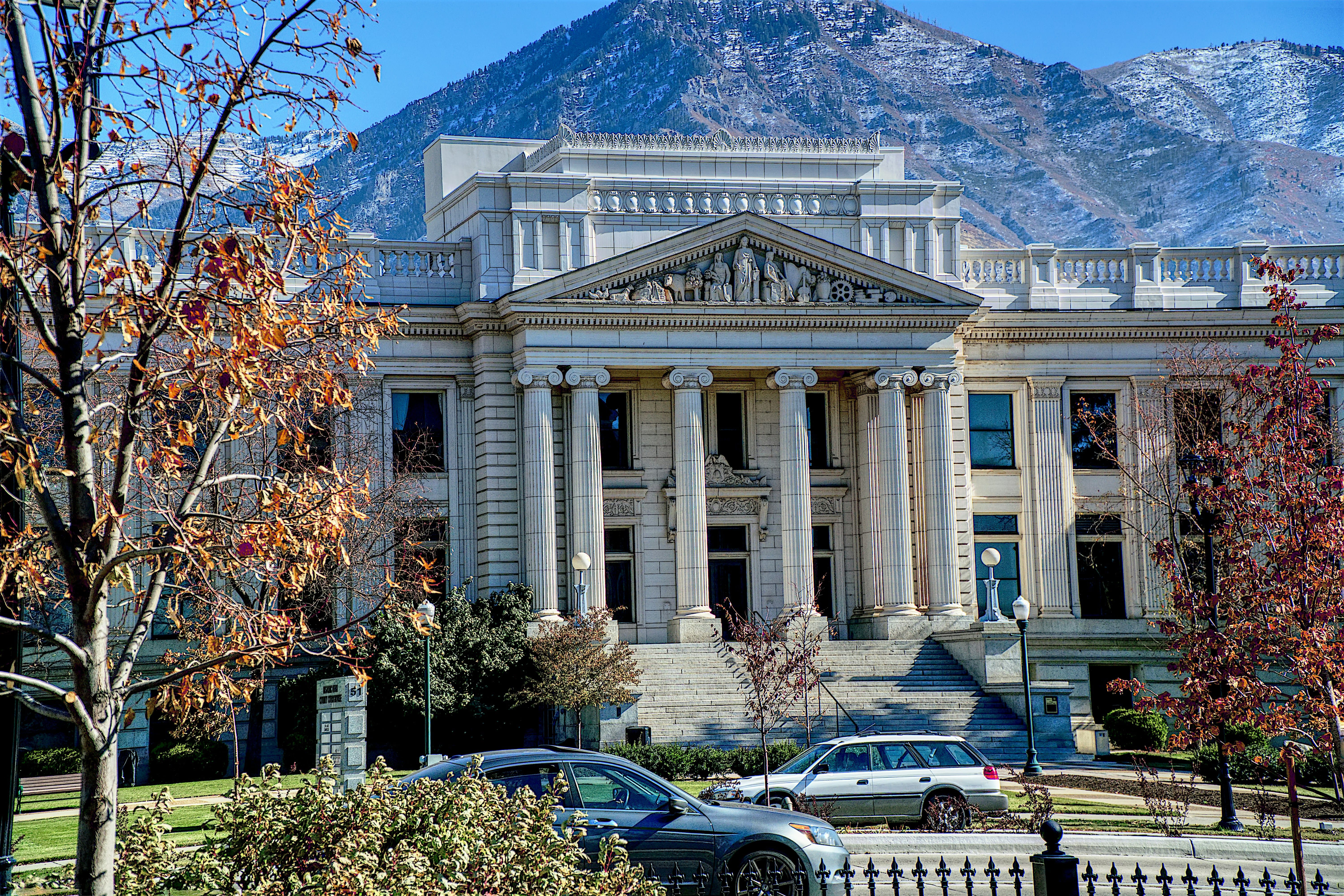 A neoclassical courthouse or Supreme Court building with white marble columns and a triangular pediment, photographed in landscape orientation on a clear day with mountains visible in the background and autumn foliage in the foreground.