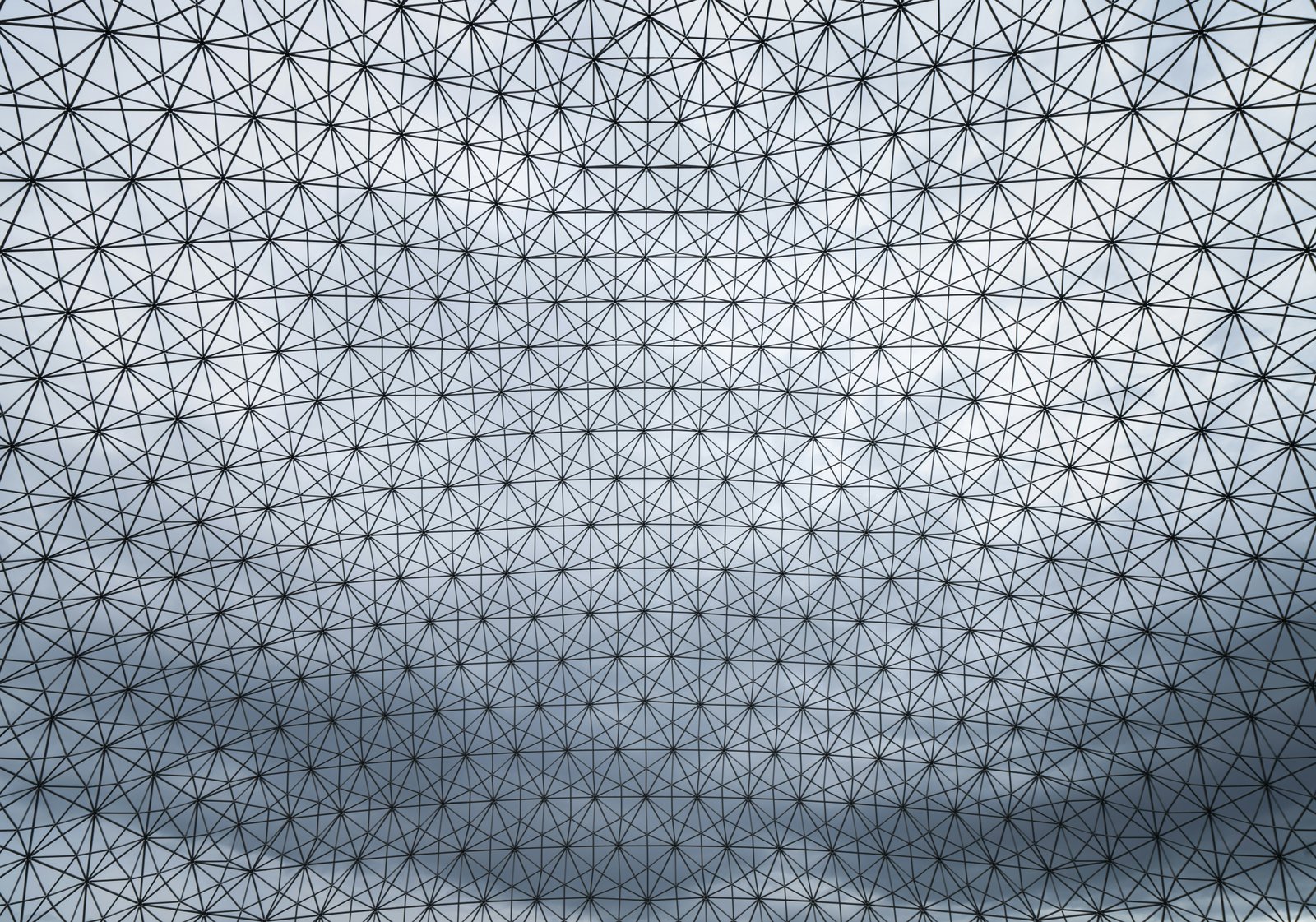 A close-up view of an intricate geometric grid pattern composed of interconnected triangular lines creating a three-dimensional mesh structure against a dark gradient background, suggesting mathematical abstraction and digital visualization.